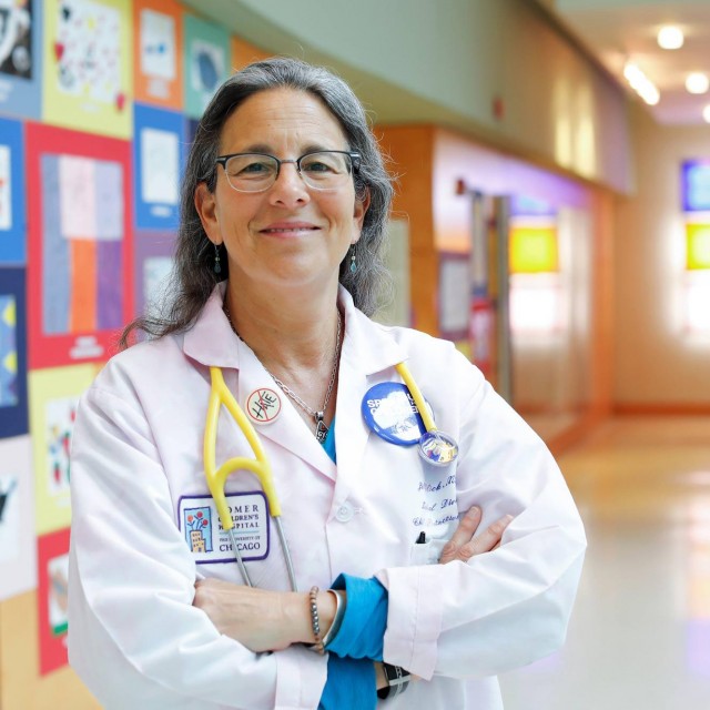 Jill C. Glick, MD, stands in hallway with children's drawings behind her